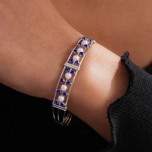 Eleganter silberner Armreif mit blauen Strasssteinen und weißen Perlen am Handgelenk