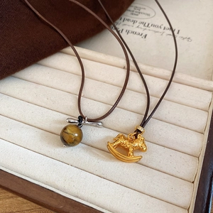 Detailed close-up of tiger eye stone and golden rocking horse pendant on woven wax cord chain