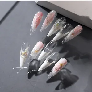 Detailed view of pink and white gradient stiletto nails with pearls and butterfly art