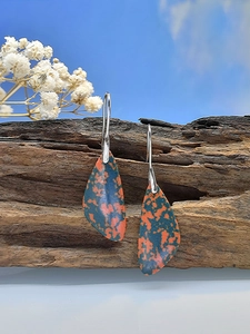 Macro detail of teardrop turquoise earrings resting on weathered wood with nature backdrop