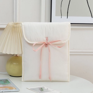 Detail of cream quilted 13-inch laptop sleeve with pink ribbon bow on a stylish desk