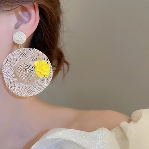 Detail view of woven straw hat earrings with yellow flower pendant on model