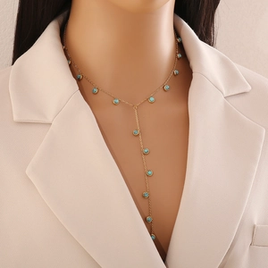 Détail d'un collier en Y doré avec gemmes turquoise sur fond de blazer beige crème