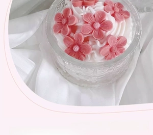 Top view of cake-shaped scented candle with pink 3D floral wax decorations on white silk