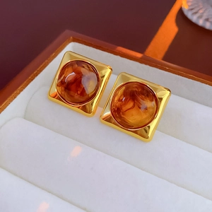 Detail of square gold metal earrings with amber resin inset on white velvet display