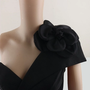 Detail of a large 3D black handmade rose brooch pinned on a black one-shoulder dress