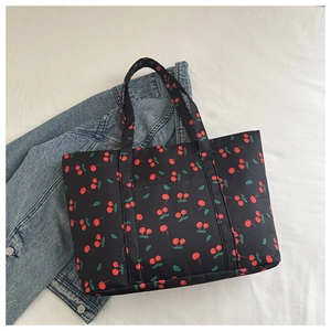 Detailed top view of black tote bag with cherry pattern next to a denim jacket