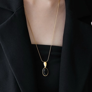 Chic gold snake chain with black oval resin pendant on a professional black suit background