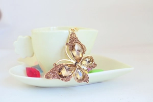 Macro detail of gold butterfly keychain with champagne crystals on a ceramic cup