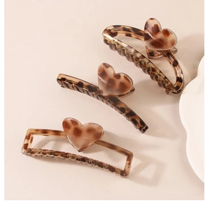 Detailed view of three leopard print hair claws with 3D heart accents on beige backdrop