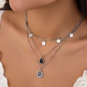 Detail of layered silver necklaces with black teardrop pendant and vintage coin charm