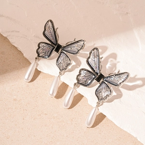 Macro shot of silver butterfly long earrings with teardrop pearls on a stone texture base