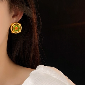 Close-up of vintage gold stud earrings with green and orange gemstones worn by a model