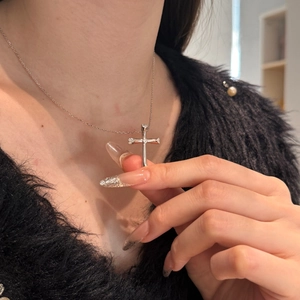 Macro close-up of a silver cross pendant necklace with inlaid zircon on a model's neck