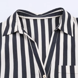 Close-up of a striped button-down shirt featuring black vertical stripes and a gold button
