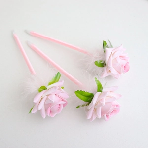 Three creative pink rose flower ballpoint pens with elegant white feathers on white backdrop