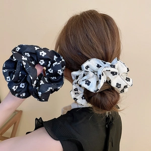 Detailed view of large floral fabric scrunchies in black and white worn on a ponytail