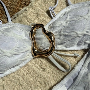 Close-up of white bikini top with embossed texture and gold irregular metal buckle