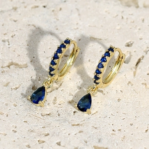 Dettaglio di orecchini a cerchio dorati con zircone blu a goccia e micro-pavé