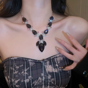Close-up of a teardrop-shaped blue gem necklace set with pink crystals on a model