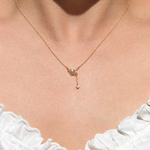 Golden heart necklace with star pendant and tassel worn on a model neckline
