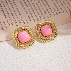 Macro shot of vintage gold earrings with pink square resin stones on textured fabric
