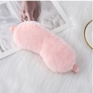 Close-up of soft pink plush eye mask with satin elastic strap on a cozy background