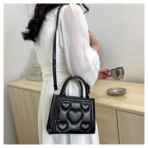 Gros plan d'un sac bandoulière noir avec motifs de cœurs embossés et détails de couture