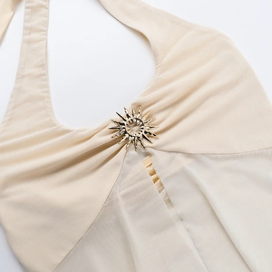 Detail van gouden zonmetaalornament op beige haltertops met transparante geplooide gaas