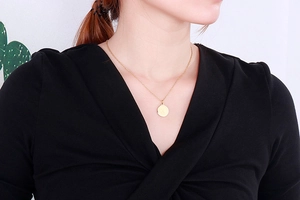 Gros plan d'un collier médaille doré avec lettre X porté par un mannequin en col en V