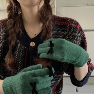 Detail of dark green knit gloves with black velvet bow on hand with vintage cardigan
