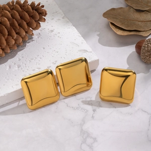 Close-up of three 18K gold-plated square earrings on a marble surface with natural decor