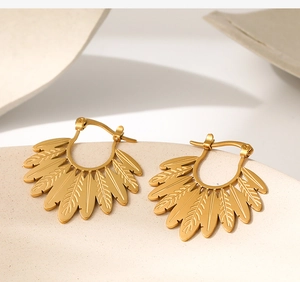 Macro detail of golden leaf feather earrings on a textured minimalist pedestal