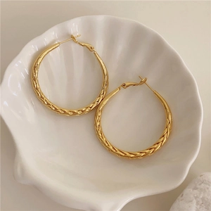 Detailed view of golden twisted metal hoop earrings resting on a white shell tray
