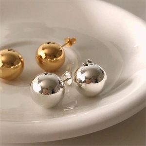 Macro view of gold and silver S925 sterling silver ball earrings on a white ceramic plate