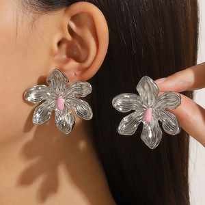 Close-up of oversized silver metal flower earrings with pink enamel center on ear