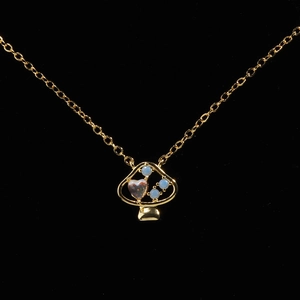 Collana con ciondolo a fungo dorato con opale a cuore e zirconi blu su sfondo nero