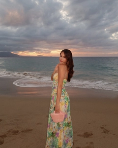 Maxikleid mit Blumenmuster, Taillierung und rosa geflochtener Handtasche am Strand bei Sonnenuntergang