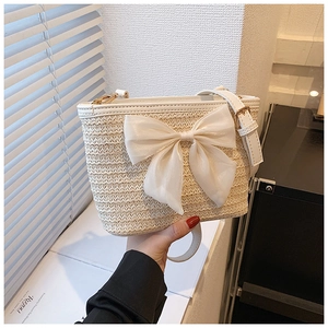 Detailed shot of woven straw bucket bag with large white chiffon bow and leather strap