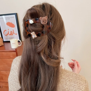 Detail of tortoise shell hair clip with plush bears and pearls on dark wavy hair
