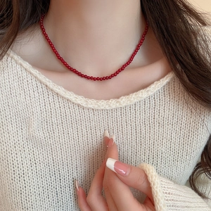 Close-up of minimalist deep red glass bead necklace on a beige knit sweater background