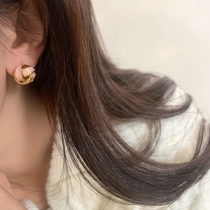 Close-up of retro pink and gold knot earrings worn on ear showing elegant weaving details