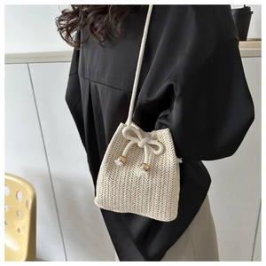 Detail of hand-woven beige straw bucket bag with drawstring closure and metal tips