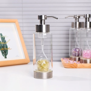 Glass soap dispenser with yellow crystal stones and stainless steel pump on a wooden desk