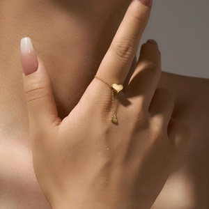 Macro detail of gold heart tassel chain ring featuring a dangling mini heart charm