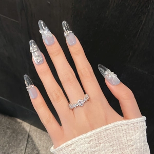 Detail of blue cat-eye press-on nails with 3D butterfly charms and sparkling rhinestones