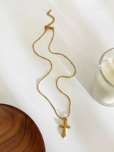 Detail of a gold-plated cross pendant with delicate beaded chain on minimalist white background