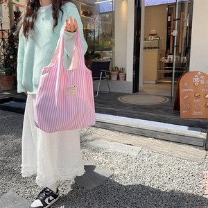 Detail of pink striped canvas tote bag with textile patch worn with a knit sweater