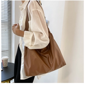 Side view of dark brown large capacity faux leather tote bag worn by a model in a minimal room