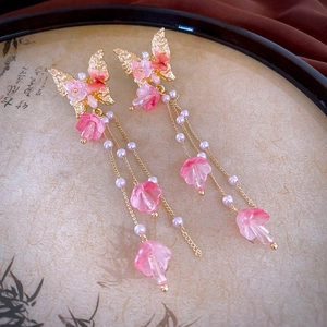 Détail de boucles d'oreilles dorées à pompons avec fleurs roses et perles sur plateau